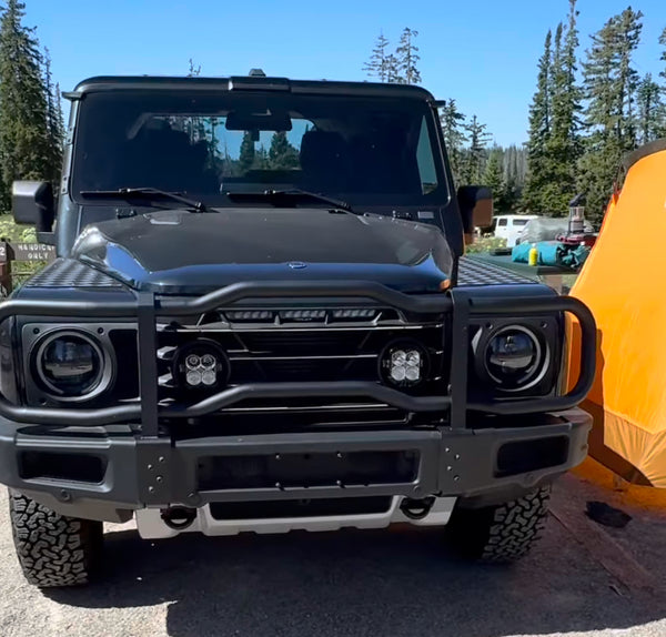 Front view of a black off-road vehicle with a clear sky and trees in the background